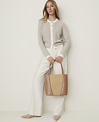 A woman in a beige cardigan and white pants holds a tan and beige tote bag in front of a plain, light-colored background. carousel Product Image 3