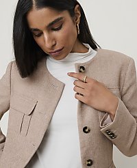 A woman in a beige tweed jacket and white turtleneck stands against a plain, light background. carousel Product Image 4
