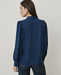 A woman in a teal blouse and dark pants stands against a plain, light gray background. carousel Product Image 2