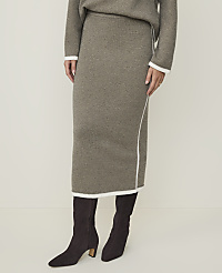 A person models a taupe knit midi skirt with white trim and dark brown boots against a plain, light background. carousel Product Image 2