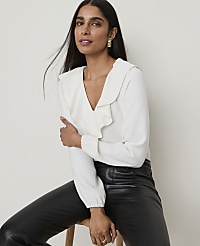 A woman in a cream ruffled blouse and black leather pants poses against a plain, light-colored background. carousel Product Image 1
