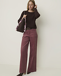 A woman in a brown sweater and pink corduroy pants stands against a plain, light-colored background, holding a tote bag. carousel Product Image 1
