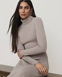 A woman in a beige turtleneck dress sits in the foreground against a plain, light-colored background. carousel Product Image 3