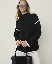 A woman in a black sweater with white trim and sunglasses holds a black tote bag in front of a plain background. carousel Product Image 1