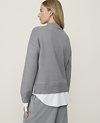 A woman in a grey sweater and white shirt stands against a plain, light grey background. carousel Product Image 2
