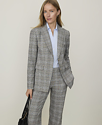 A woman in a plaid suit stands against a plain, light-colored background.