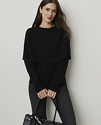A woman in a black sweater and pants stands in front of a plain background, holding a black handbag. carousel Product Image 1