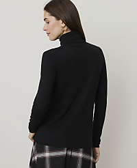 A woman in a black turtleneck sweater and plaid skirt stands against a plain, light gray background. carousel Product Image 2