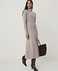 A woman in a beige turtleneck dress and brown boots stands with a dark brown tote bag against a plain, light gray background. carousel Product Image 1