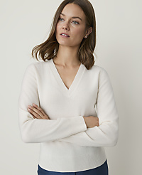 A woman in a cream v-neck sweater stands with her arms crossed against a plain, light background. carousel Product Image 1