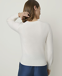 A woman in a white sweater and blue pants stands against a plain, light-colored background. carousel Product Image 2