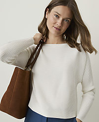 A woman in a white ribbed sweater and blue pants carries a brown tote bag against a plain background. carousel Product Image 1