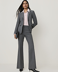 A woman in a gray pinstripe suit and pink blouse stands against a plain white background, holding a black clutch. carousel Product Image 1