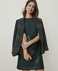 A woman in a green dress and plaid blazer holds a brown clutch in front of a plain background. carousel Product Image 3