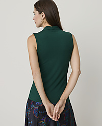 A woman in a green sleeveless top and patterned skirt stands with her hands clasped behind her back against a plain background. carousel Product Image 2