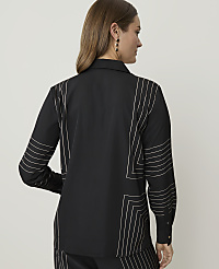 A woman in a black shirt with white geometric stitching stands against a plain white background. carousel Product Image 2
