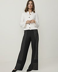A woman in a white jacket and black patterned pants stands against a plain white background. carousel Product Image 4