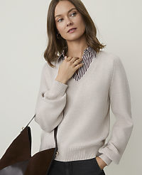 A woman in a cream v-neck sweater over a striped shirt stands against a plain, light background, with a brown bag in the foreground. carousel Product Image 1