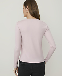 A woman in a light pink long-sleeved shirt and dark jeans stands against a plain, light gray background. carousel Product Image 2