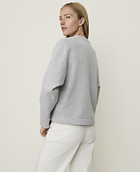 A woman in a grey sweatshirt and white pants stands against a plain, light-colored background. carousel Product Image 2