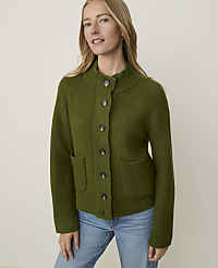 A woman in a green cardigan and jeans stands against a plain, light background. carousel Product Image 1