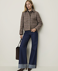 A woman in a plaid jacket and wide-leg jeans stands against a plain, light-colored wall, holding a brown tote bag. carousel Product Image 3