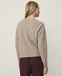 A woman in a cable-knit sweater stands against a plain, light-colored background. carousel Product Image 2