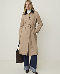 A woman in a tan trench coat and wide-leg jeans stands against a plain, light background, holding a dark tote bag. carousel Product Image 1