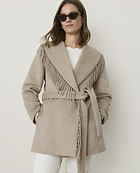A woman in a fringed beige coat stands against a plain white background. carousel Product Image 1