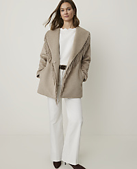 A woman in a fringed beige coat and white pants stands against a plain white background. carousel Product Image 3