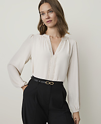 A woman in a cream blouse and black pants stands against a plain, light background. carousel Product Image 1