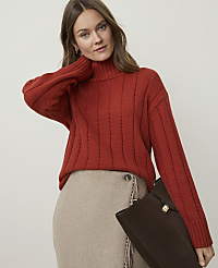 A woman in a rust-colored turtleneck sweater and a beige skirt holds a brown clutch against a plain background. carousel Product Image 1