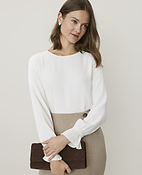 A woman in a white blouse and tan skirt holds a brown clutch in front of a plain background. carousel Product Image 1