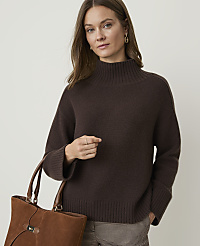 A woman in a brown turtleneck sweater and plaid pants holds a brown leather tote bag against a plain background. carousel Product Image 1