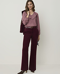 A woman in a mauve ruffled blouse and burgundy corduroy pants stands against a plain, light background, with a maroon jacket draped over her shoulder. carousel Product Image 1