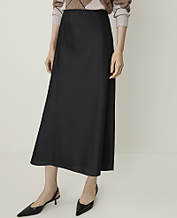 A person models a black satin midi skirt and black slingback heels against a plain white background. carousel Product Image 2