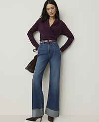 A woman in a plum-colored wrap sweater and wide-leg jeans stands against a plain white background. carousel Product Image 1