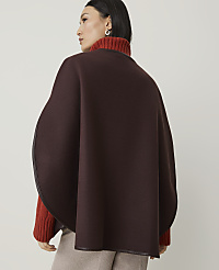 A woman in a brown cape and orange turtleneck stands against a plain, light-colored background. carousel Product Image 2