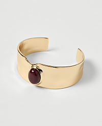 A gold cuff bracelet with a deep red stone sits on a plain white background. carousel Product Image 1