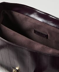 A glossy, dark purple handbag with vertical stitching is open in the foreground, revealing its brown fabric lining and a small brand tag, against a plain, light background. carousel Product Image 2