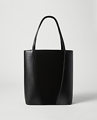 A sleek black leather tote bag with a V-shaped seam stands against a plain, light gray background. carousel Product Image 1