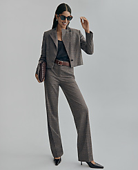 A woman in a plaid suit and sunglasses poses with a clutch bag against a plain gray background.