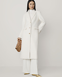 A woman in a white coat and wide-leg pants holds a tiger-print clutch against a plain white background. carousel Product Image 1