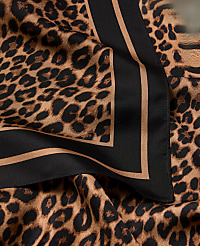 A close-up of a leopard print scarf with a black and tan border is draped over a matching fabric. carousel Product Image 2