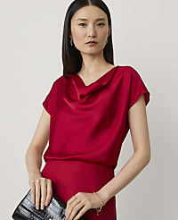 A woman in a red cowl-neck top and holding a black clutch stands against a plain white background. carousel Product Image 1