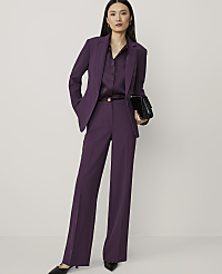 A woman in a purple pantsuit stands against a plain white background, holding a black clutch. carousel Product Image 3