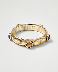 A gold ribbed bangle with four colorful cabochon stones is displayed against a plain white background. carousel Product Image 1