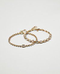 Two delicate gold bracelets, one with a simple chain and the other adorned with clear stones, rest against a plain white background. carousel Product Image 1