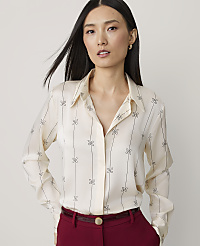 A woman with dark hair and a patterned cream blouse stands against a plain background. carousel Product Image 1