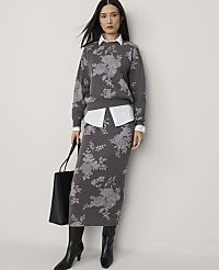A woman in a floral sweater and skirt stands against a plain background, holding a black tote bag. carousel Product Image 1
